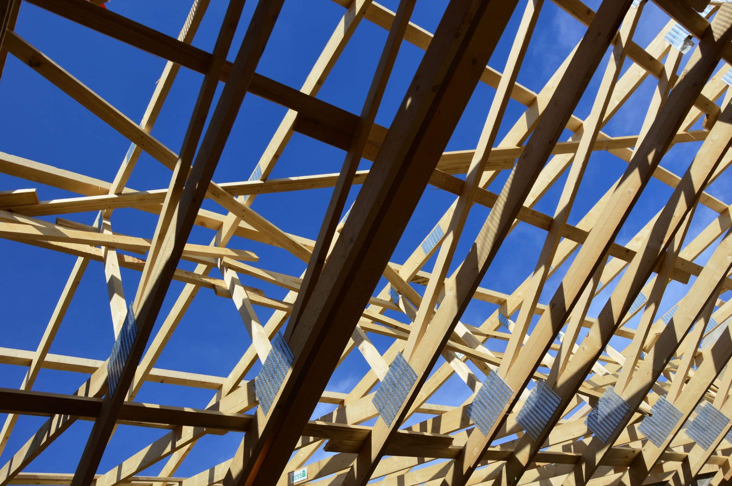 Timber roof trusses under construction against a blue sky