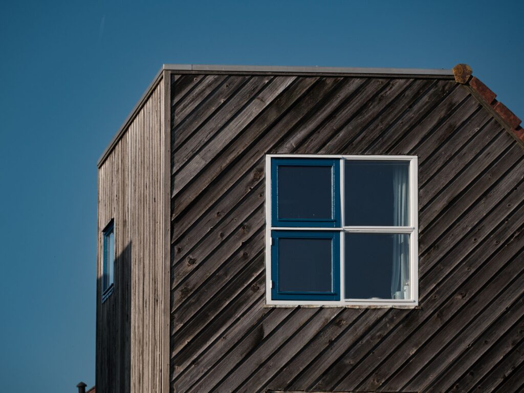 Dark timber-clad house corner with a large window against a clear sky