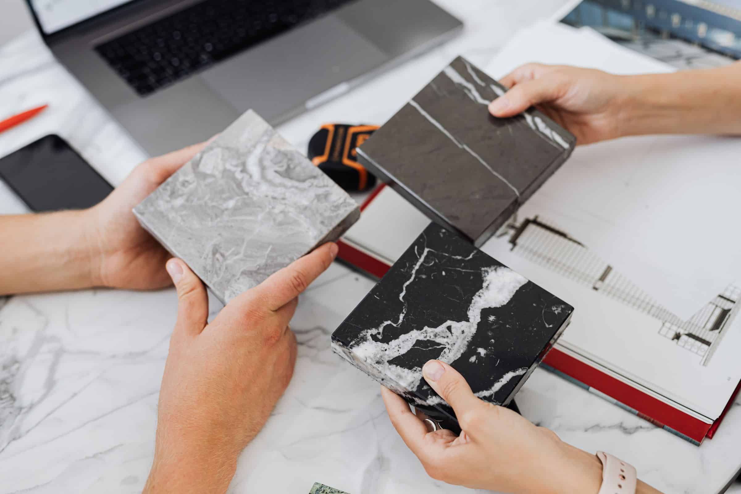 Hands reviewing material samples of stone and tile on a work surface
