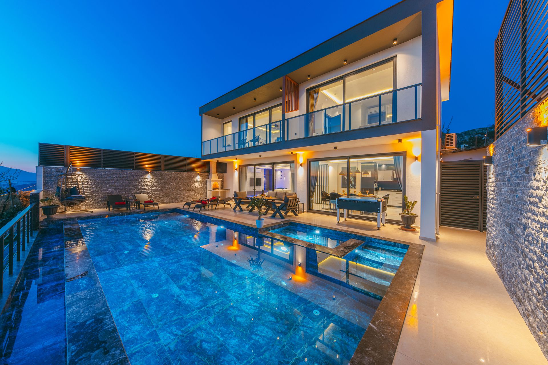Modern stone-and-glass residence with an illuminated pool terrace at dusk — representative architecture