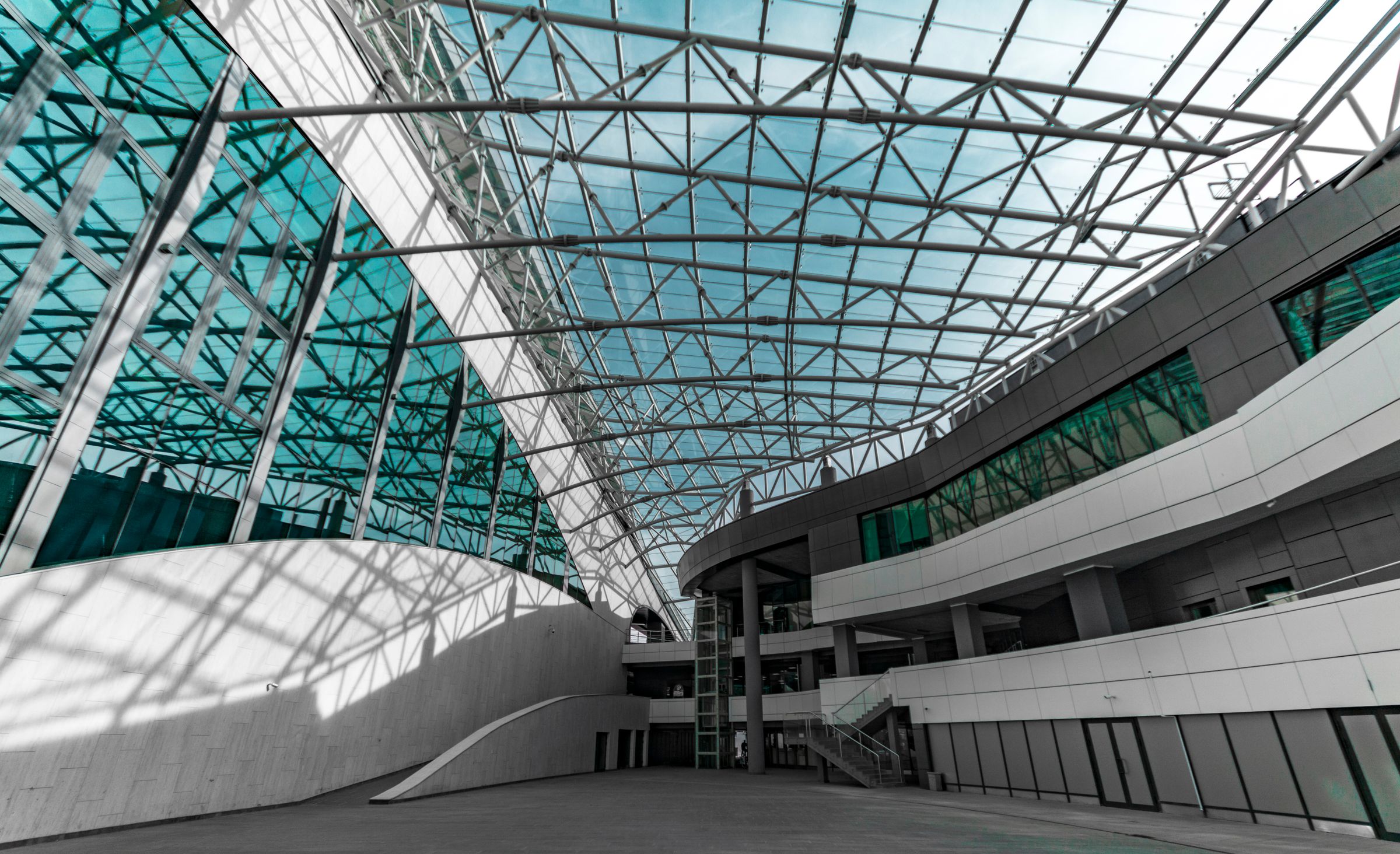 Steel and glass atrium roof structure with layered trusses in daylight