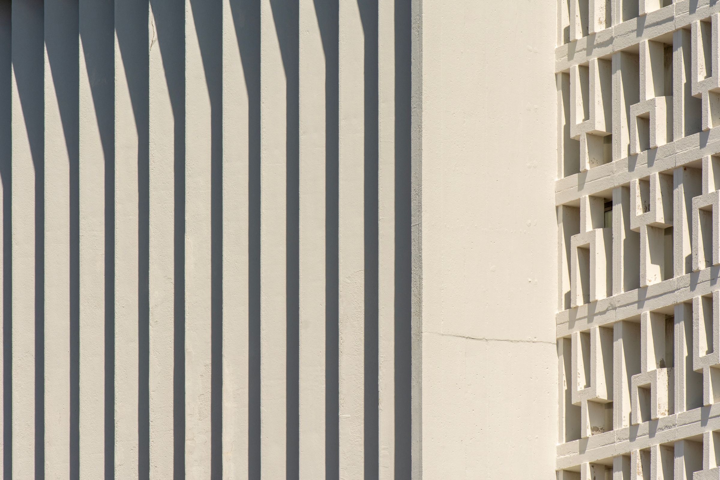 Sunlit facade with rhythmic vertical shadow stripes across light panelling