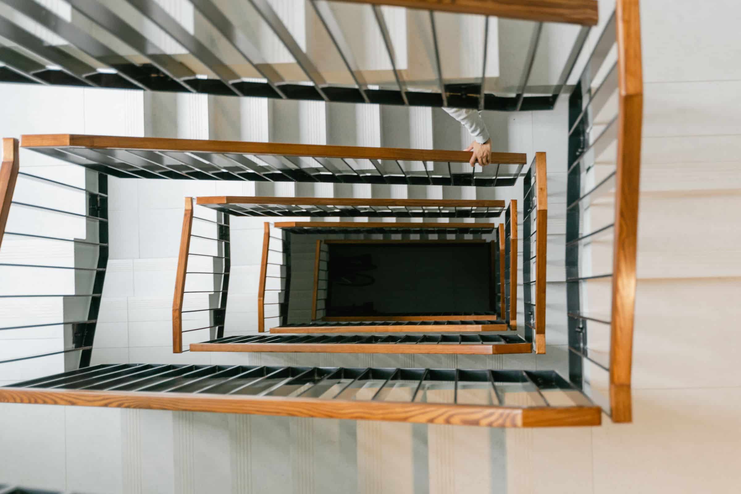 Overhead view of a wooden staircase with layered handrails and soft light